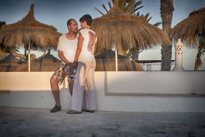 Full length of couple romancing by retaining wall against thatched roofs