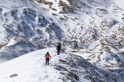 From above of unrecognizable explorers with hiking sticks walking through rough rocky pyrenees mountain range covered with snow