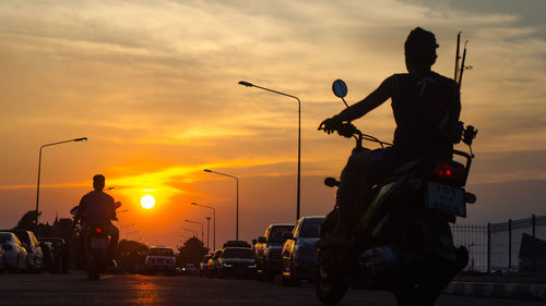 Rear view of men driving motorcycles against sky during sunset