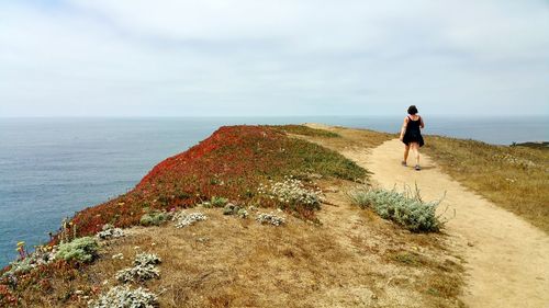 Rear view of woman on dirt road against sea and sky