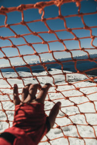 Cropped hand of woman holding net against sky during winter