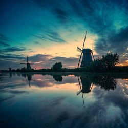 Traditional windmill by lake against sky during sunset