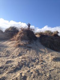 Boy standing on grassy sand dunes at beach against sky