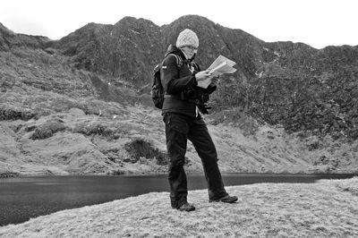 Full length of hiker looking at map near lake against mountains