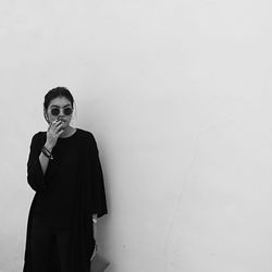 Young woman smoking cigarette while standing against wall