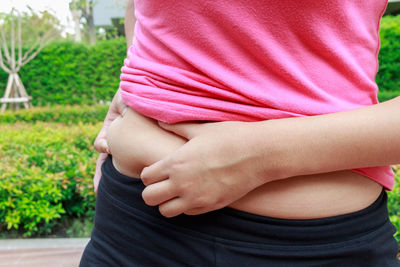 Midsection of woman holding belly while standing outdoors