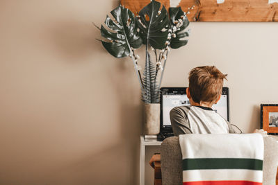 Rear view of boy learning on laptop while sitting on chair at home