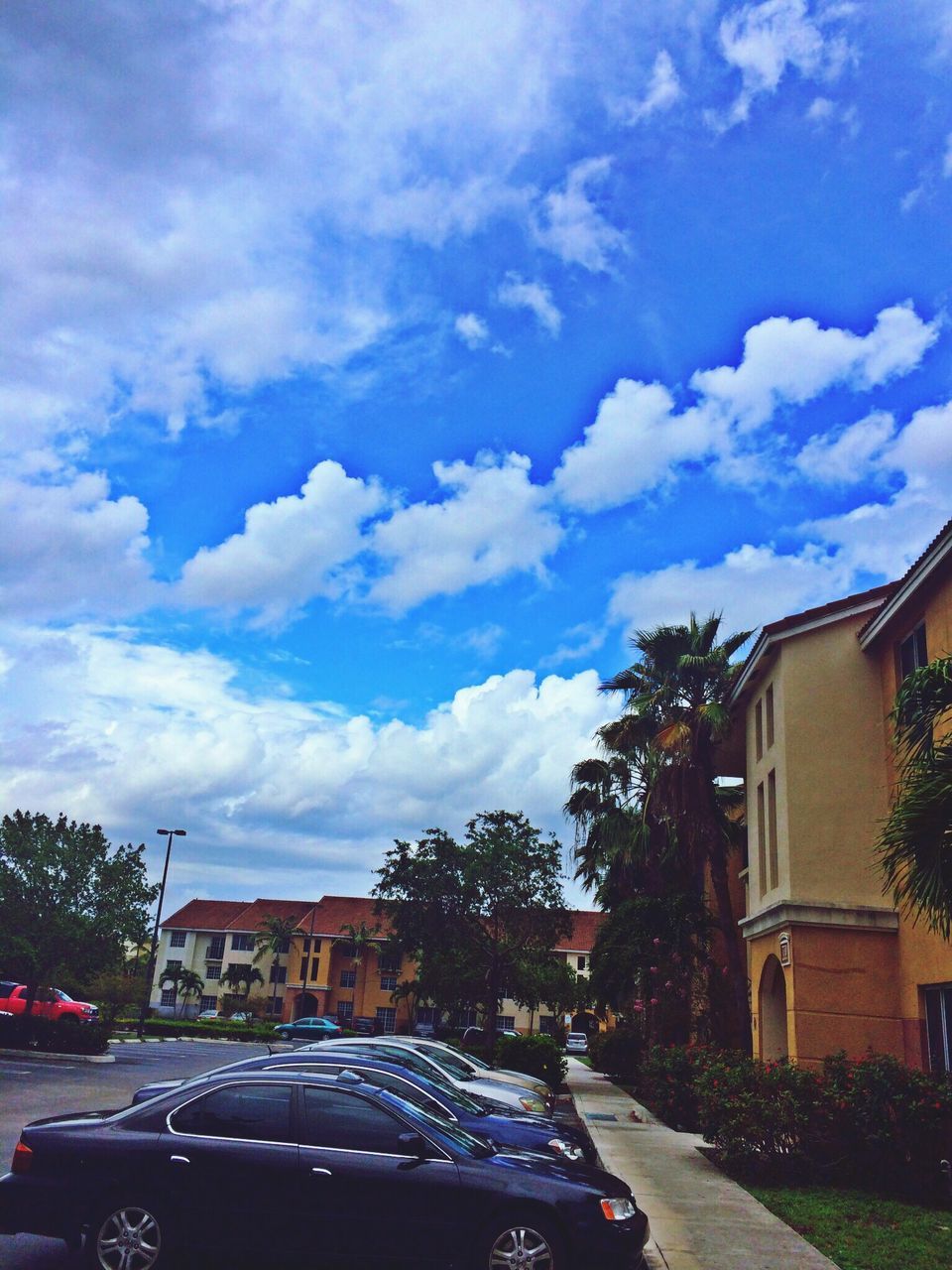 car, building exterior, transportation, land vehicle, architecture, sky, built structure, tree, mode of transport, street, road, cloud - sky, house, city, cloud, residential building, parking, cloudy, residential structure, outdoors