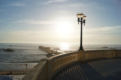 Street light by sea against sky during sunset