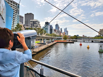 Man holding railing by river against buildings in city