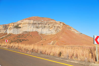 Road leading towards mountain against clear blue sky