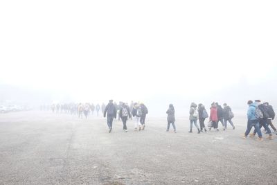 People walking on road against sky during foggy weather
