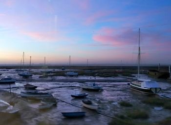 Sailboats moored on harbor against sky during sunset