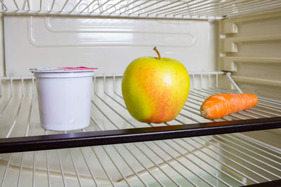 Apple with container and carrot on shelf in refrigerator
