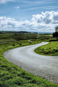 Road passing through field against cloudy sky