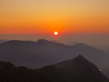 Scenic view of silhouette mountains against orange sky