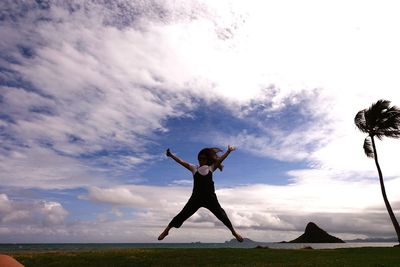 Woman jumping at beach against cloudy sky