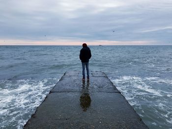 Rear view of man standing on jetty against sea at beach