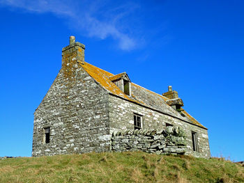Low angle view of old cottage building against blue sky