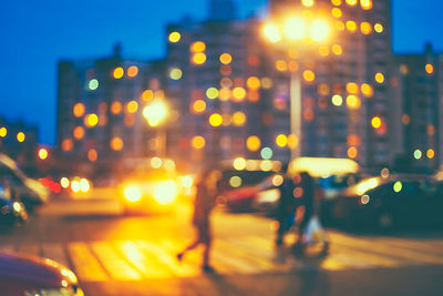 Defocused image of illuminated city street against sky at night