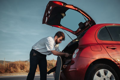 Rear view of man standing by car against sky