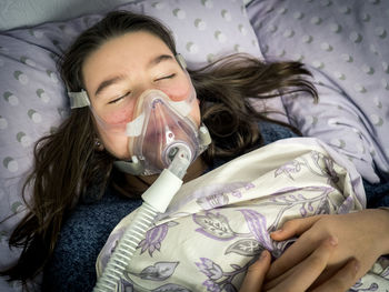 High angle view of woman wearing oxygen mask while sleeping on bed