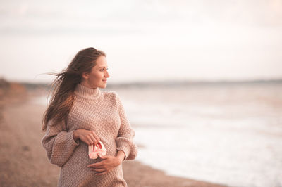 Pregnant woman holding baby shoe standing at beach