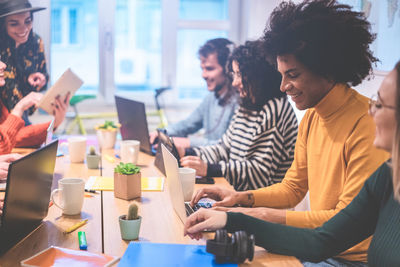 Business people using laptops on table while sitting in creative office