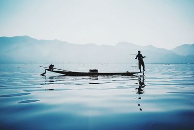 Man fishing in lake against clear sky