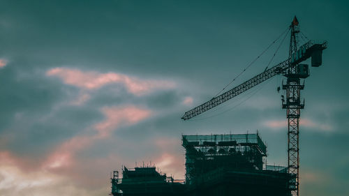 Low angle view of crane by building against sky