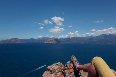 Low section of woman relaxing on rock formations by sea against sky
