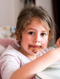 Close-up portrait of cute girl with cake on her face at home