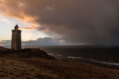 Lighthouse on beach by sea against sky