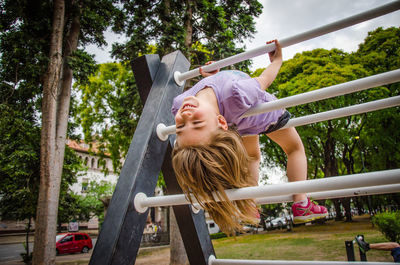 Low angle view of girl hanging on structure at park