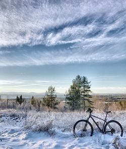 Bicycle on snow covered landscape against sky