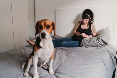 Young woman with dog sitting on bed at home