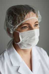 Doctor wearing mask and surgical cap against gray background