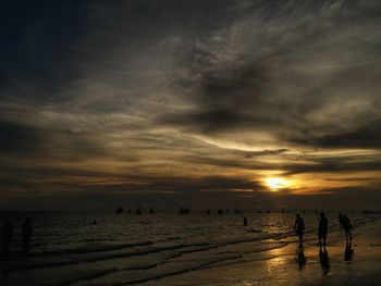 Silhouette people on beach against sky during sunset