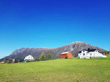 House on field by houses against clear blue sky