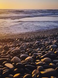Pebbles on beach against sky during sunset