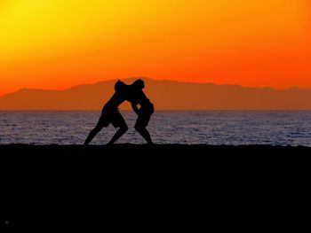 Silhouette woman standing on sea against orange sky