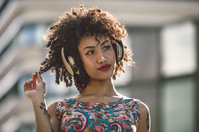 Fashionable young woman with curly hair listening music in city