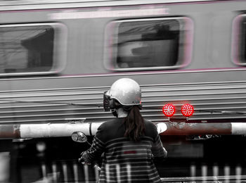 Rear view of woman riding motor scooter against train