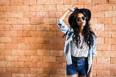 Portrait of woman wearing sunglasses while standing by brick wall