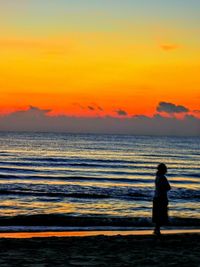 Rear view of silhouette woman standing at beach during sunset