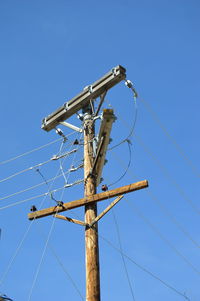 Low angle view of electricity pylon against clear blue sky