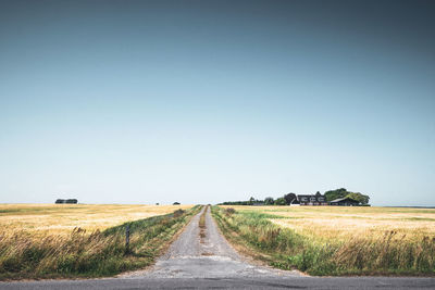 Empty road amidst field against clear sky