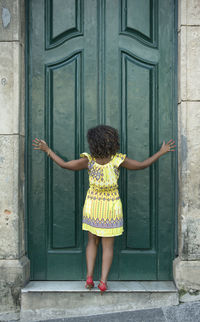 Portrait of young woman standing against door