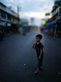 Boy holding ice cream cone on road in city