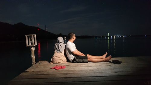Rear view of men sitting on pier at night